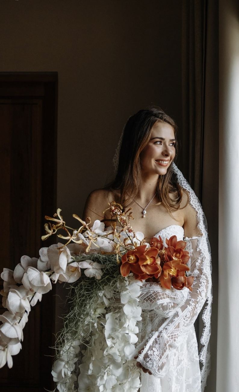 Bride by a window holding a trailing bouquet